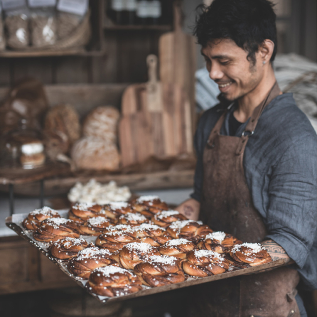 En man står med en plåt fylld med nybakta kanelbullar