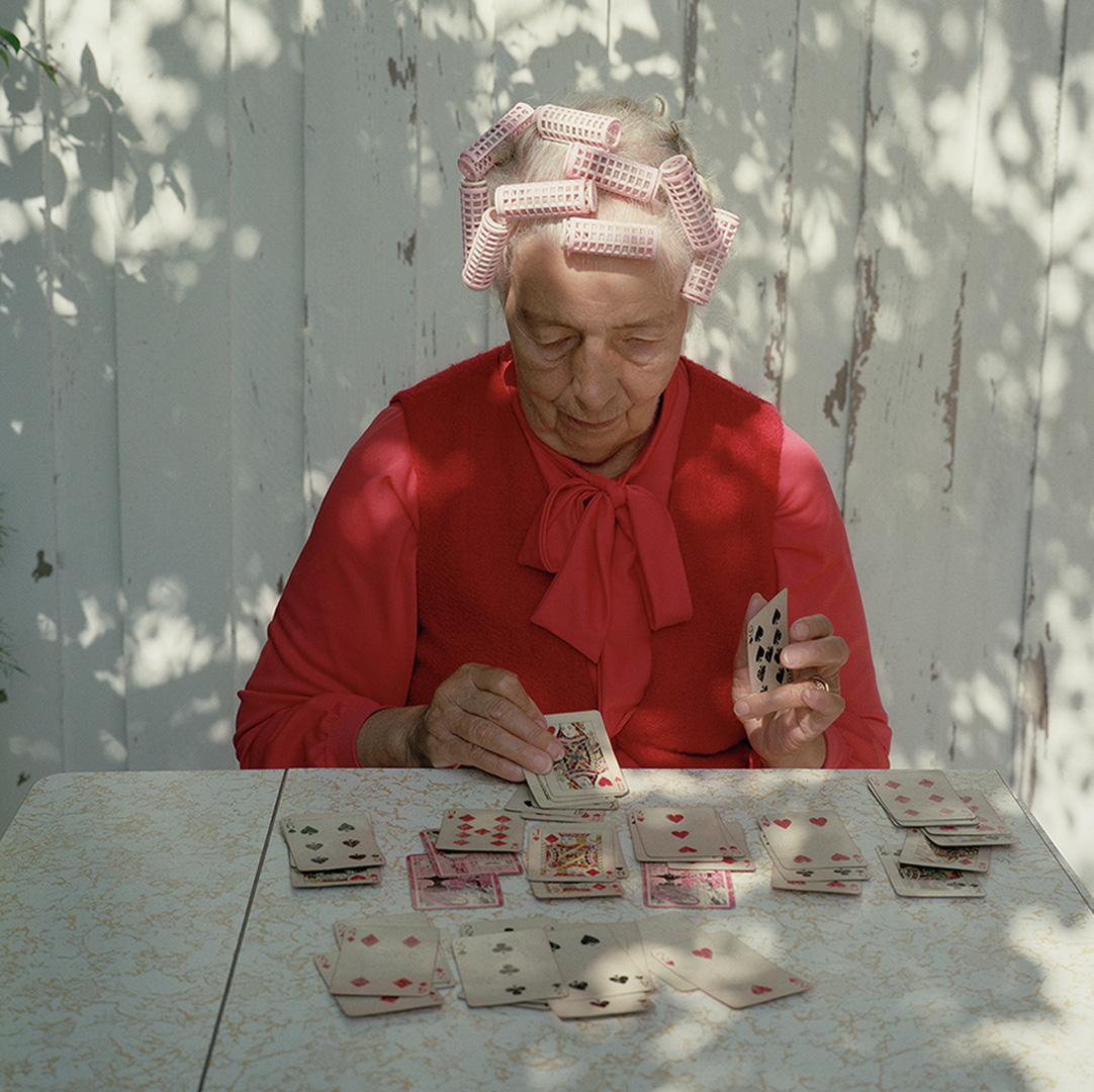 dam med papiljotter och röd stickad tröja spelar kort