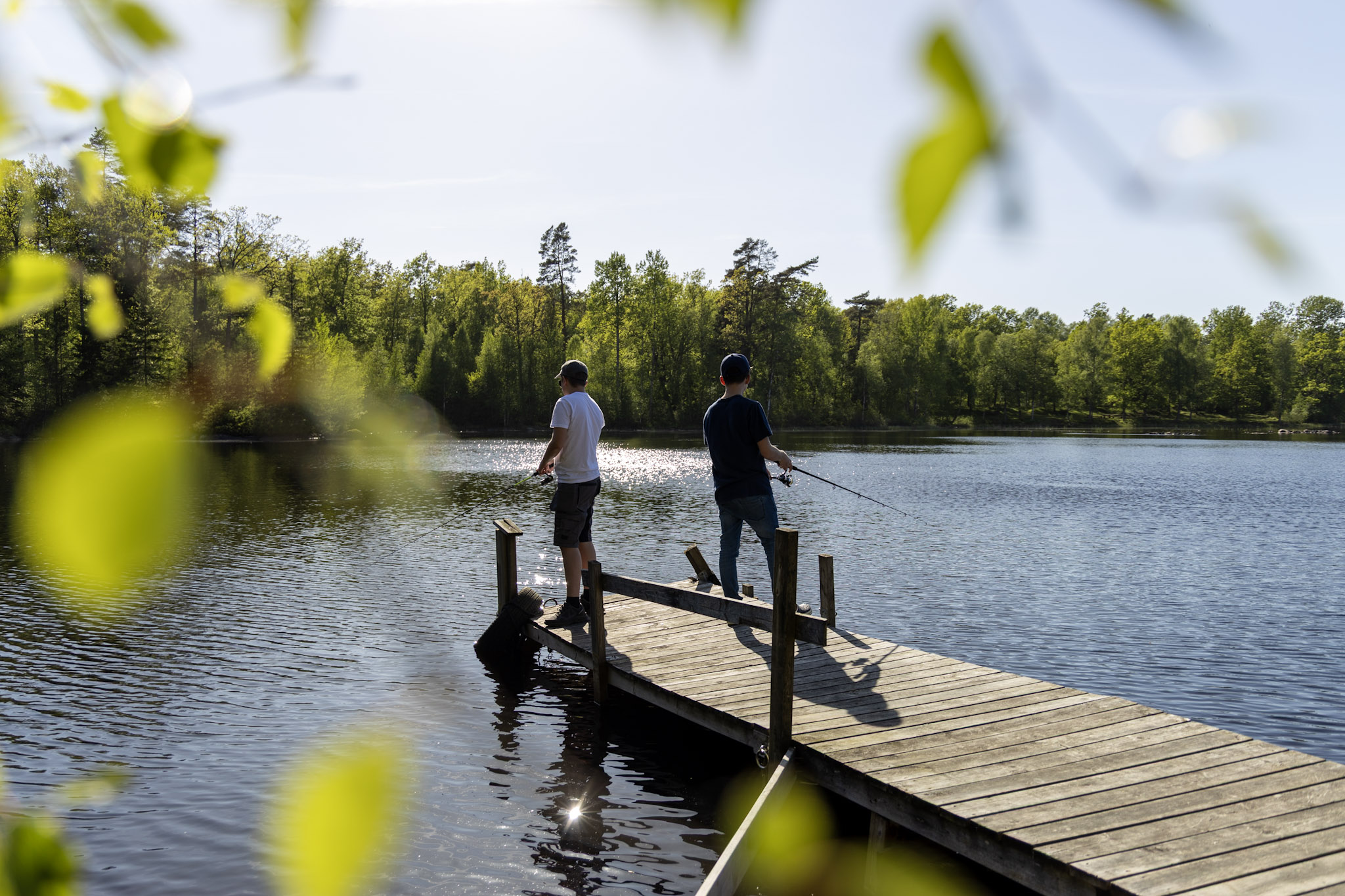 Två killar fiskar på en brygga i en sjö.